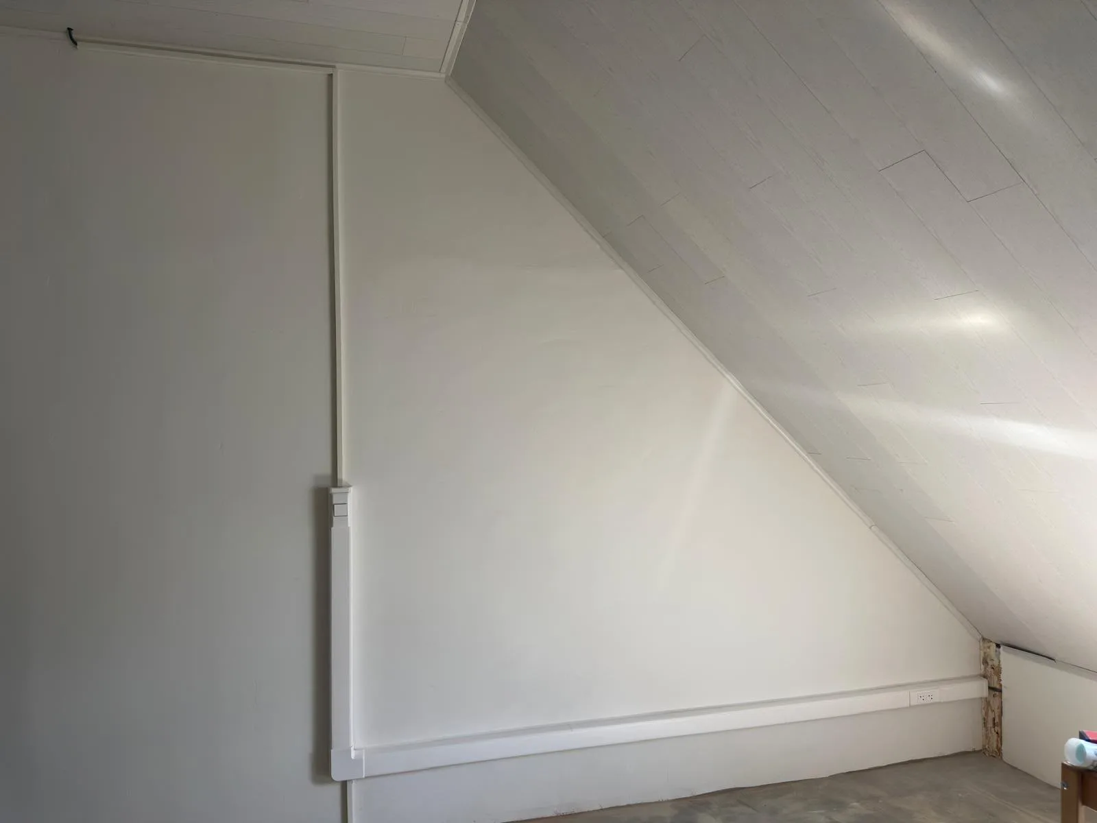 Zolderkamer met een witte plintgoot en een verticale goot naar de schakelaar, strak langs de muur